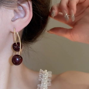 Minimalist dark red resin cherry stud earrings with gold curved stem on female model