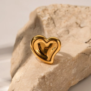 Close-up of an 18K gold heart ring on a natural rock with a polished metallic finish