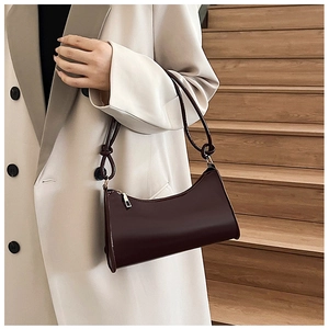 Detail of dark brown glossy leather baguette bag with top zipper and slim shoulder strap