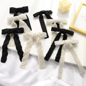 Handmade beaded bow hair clips with pearls in black and cream on minimalist pedestals
