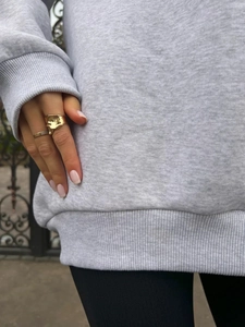 Close-up of golden irregular lava texture and pavé band rings worn on a hand over gray fabric