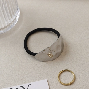 Detail of black elastic hair tie with irregular silver metal plate and gold accent piece