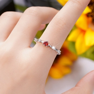 Detail of a romantic heart-shaped red zircon ring with twisted silver band on finger