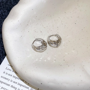 Macro shot of silver C-shaped pleated earrings on a ceramic dish with soft lighting