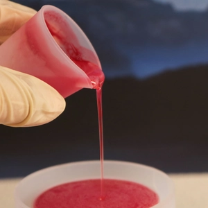 Makroaufnahme von rotem Harz beim Gießen aus einem 30ml Silikon-Messbecher mit Skala