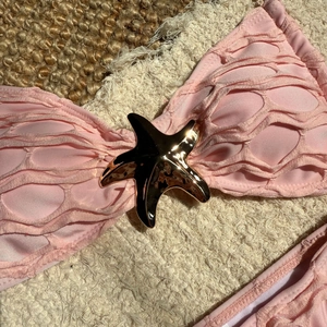 Close-up of pink bikini top with textured fabric and golden starfish metal buckle detail