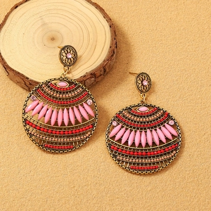 Detail of bohemian gold earrings featuring pink and red beaded tassels on sandy background