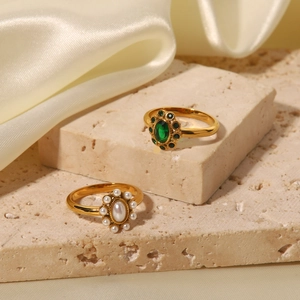 Close-up of gold rings featuring an emerald green gemstone and a white pearl on stone