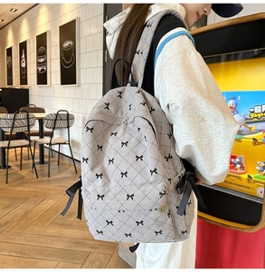Detailed side view of grey corduroy backpack featuring black bow patterns and ribbon ties
