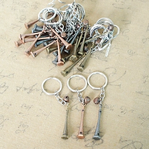 Three lighthouse-shaped metal keychains in bronze, silver and dark gray finishes with small bells