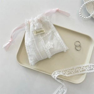 Lace drawstring pouch with pink ribbon on ceramic tray with elegant pearl accessories