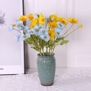 Artificial yellow and light blue poppy bouquet in a teal textured ceramic vase on lace