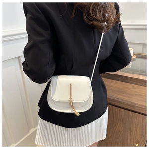 Close-up of a white leather crossbody bag with a gold tassel detail on a fashion model