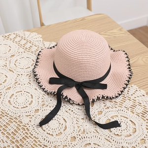 Detailed close-up of pink straw hat with black bow and wavy lace edge on a wooden table