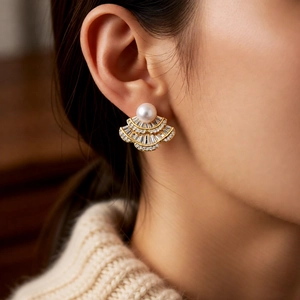 Close-up of fan-shaped pearl earrings with gold base worn by a model in warm light
