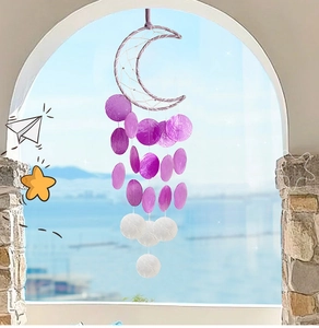 Detail of moon-shaped shell wind chime with purple and white discs on a stone window