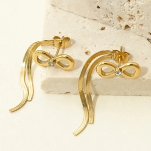 Detail of gold bow tassel earrings with small inlaid diamonds on beige stone background