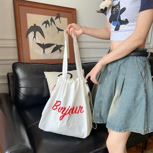 Detail of white canvas drawstring tote bag with red Bonjour print shown in a lifestyle setting