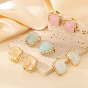 Détail de boucles d'oreilles carrées en résine rose, bleu, beige et blanc avec bord doré