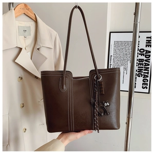 Detail of dark brown tote bag featuring white contrast stitching and a black cat charm