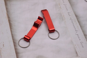 Close-up of dual red aluminum bottle openers with stainless steel keyrings on a white base