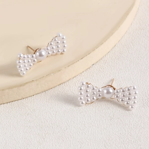 Detailed view of handmade woven bow earrings featuring white pearls and gold base