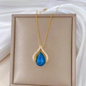 Detailed close-up of blue teardrop necklace in gold setting inside a beige jewelry box
