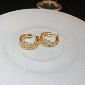 Detail of twisted gold hoop earrings with multi-wire texture on a minimalist plate