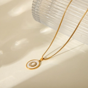 Macro shot of 18K gold plated box chain and oval white shell pendant with letter O crystal