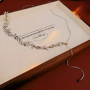 Detail of silver snake chain necklace with leaf pendants on a wooden jewelry box
