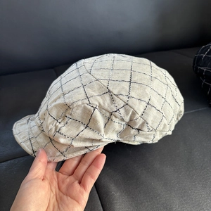 Detail of light beige plaid newsboy cap showing linen fabric texture and grid pattern