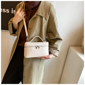 Detail of off-white lychee texture leather handbag with handle held by a model in a trench coat