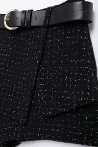 Détail du tissu en tweed noir aux fils argentés et ceinture en cuir à boucle dorée