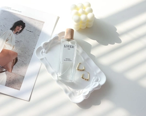 Flat lay of perfume bottle and golden earrings on white bow tray with artistic shadows