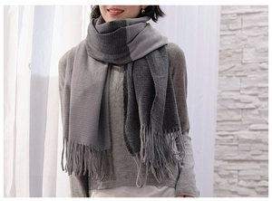 Detail of soft knit grey gradient scarf featuring fringe tassels and bicolored texture