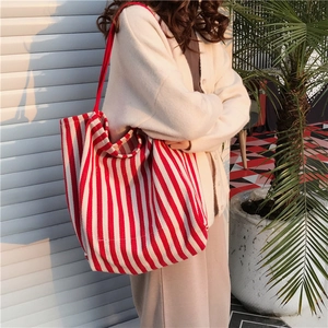 Detailed shot of large red striped canvas tote bag worn on shoulder in warm natural light