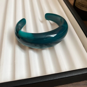 Detailed view of wide dark green acrylic bangle on white textured display stand