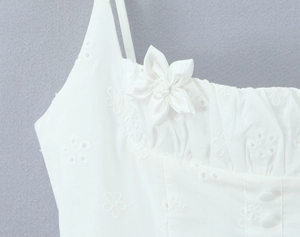 Detailed close-up of delicate floral embroidery and 3D fabric flower on white strap dress