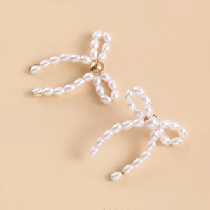 Detail of handmade bow earrings featuring woven white pearls and golden metallic accents