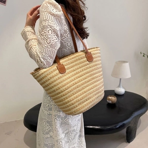 Detail of handwoven straw tote bag with brown leather handles worn by a female model