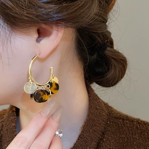 Close-up of model wearing gold hoop earrings with leopard print resin pendants