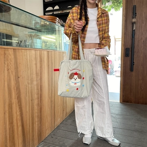 Detailed view of grey canvas tote bag with puppy embroidery held by model in cafe setting