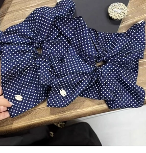 Detail view of two navy blue polka dot bow scrunchies with shell buckles on wood
