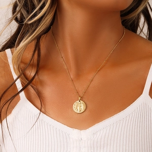 Close-up of model wearing a gold zodiac coin necklace with a relief pendant detail