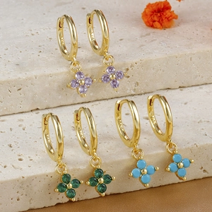 Three pairs of gold clover earrings with purple and green stones on stone podiums