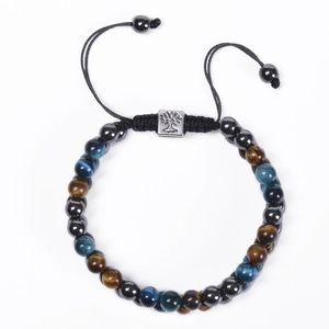 Macro detail of 8mm blue tiger eye beads and tree of life charm on braided bracelet