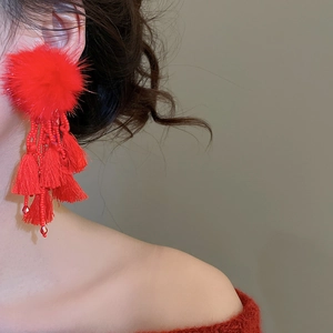 Detail shot of long red pom-pom tassel earrings with crystal beads worn by a model
