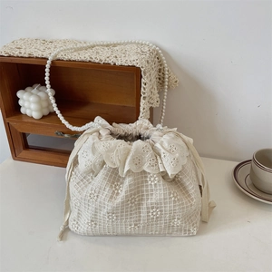 Detailansicht der cremefarbenen Spitzenbeuteltasche mit Blumenstickerei und Perlenkette