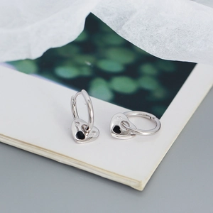 Detail shot of heart-shaped silver earrings on an open book with green plants