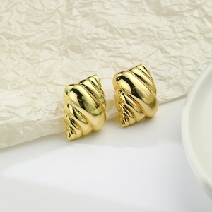 Macro detail of gold-plated spiral conch earrings on textured white background